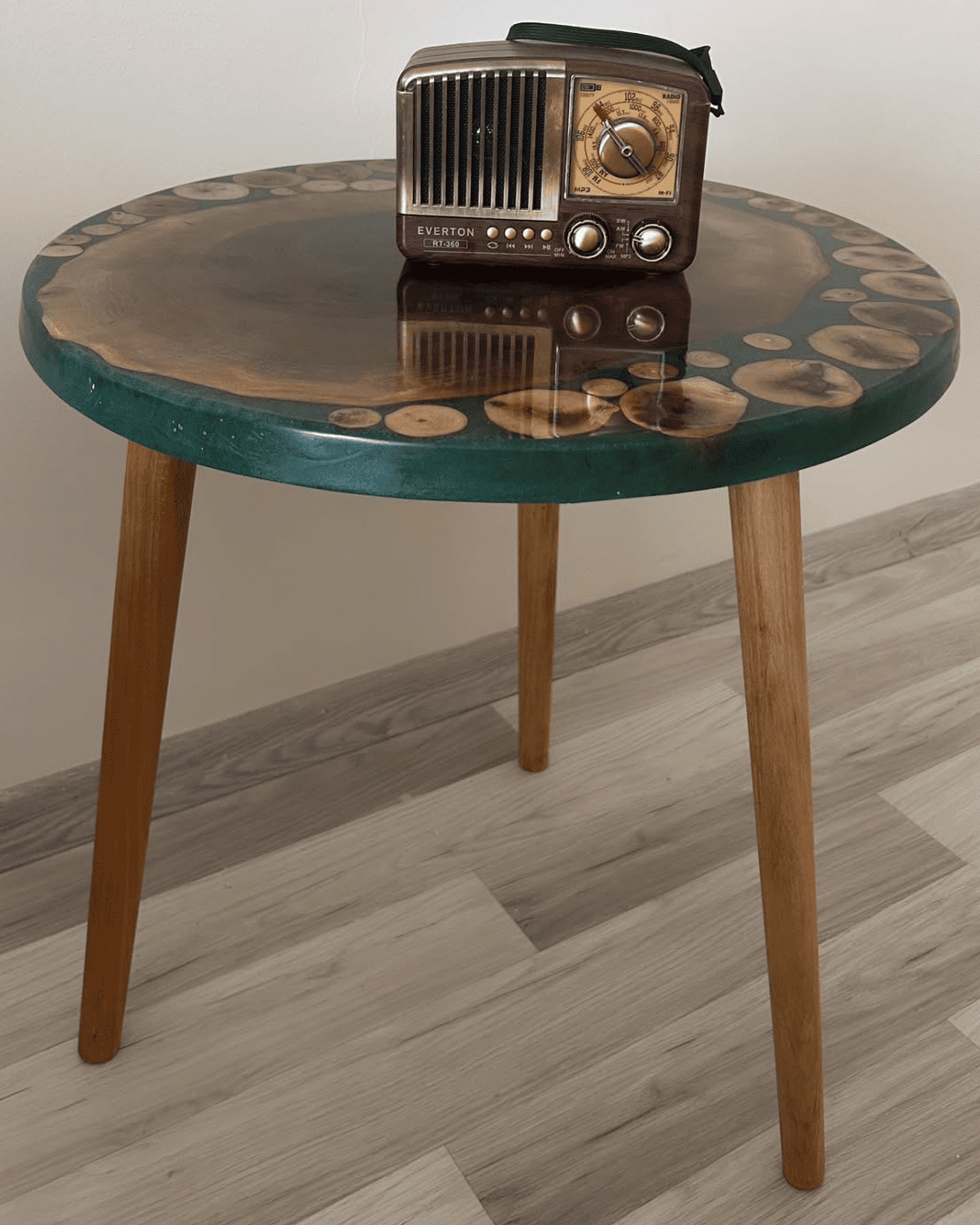 Round wooden table with a green top and a vintage radio on it, against a plain wall.