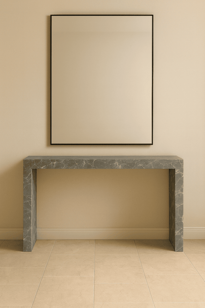 Gray marble console table against a beige wall with a framed mirror above it.