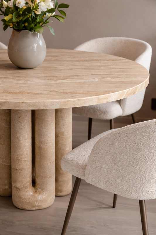 Round travertine table with marble-like legs in a dining room setting.