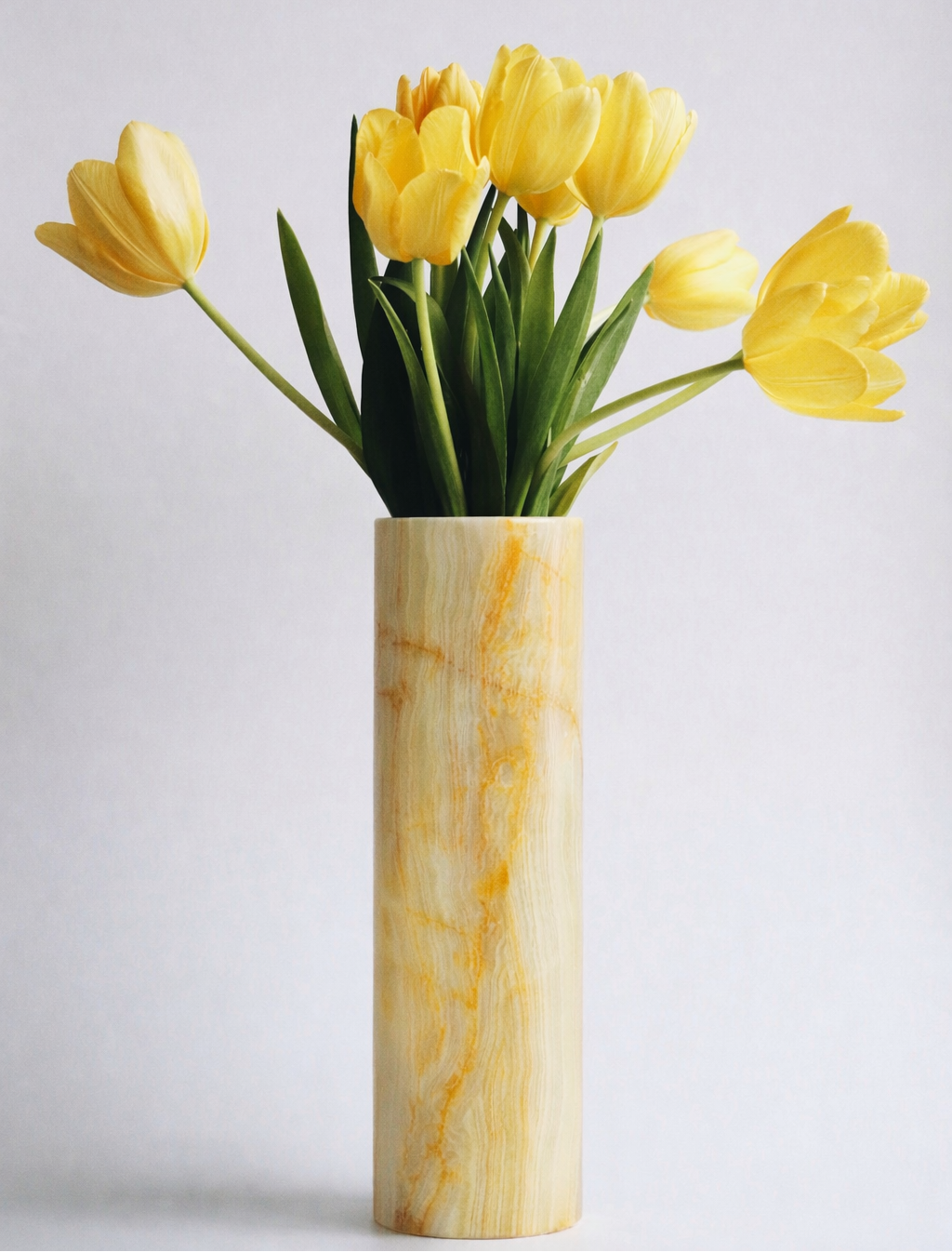 Yellow tulips in a marble vase on a light gray background